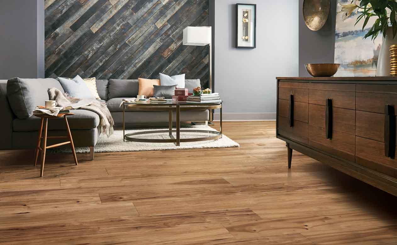 hardwood flooring and wood paneling on accent wall in living area with large grary sectional